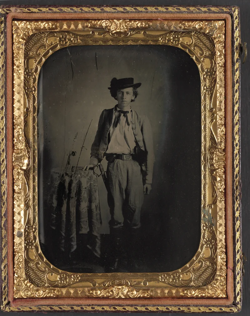 Ambrotype in an ornate gilt frame of a young man in a plumed hat and short jacket, one hand on a sabre hilt resting on a draped table, a revolver holster at his belt.